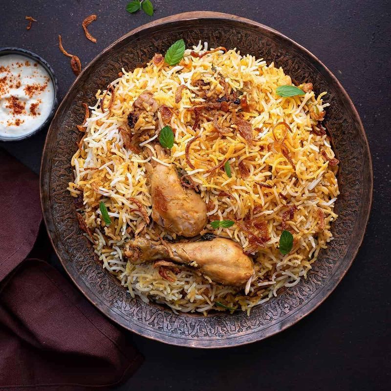 Dum chicken biryani in an engraved copper bowl served with raita